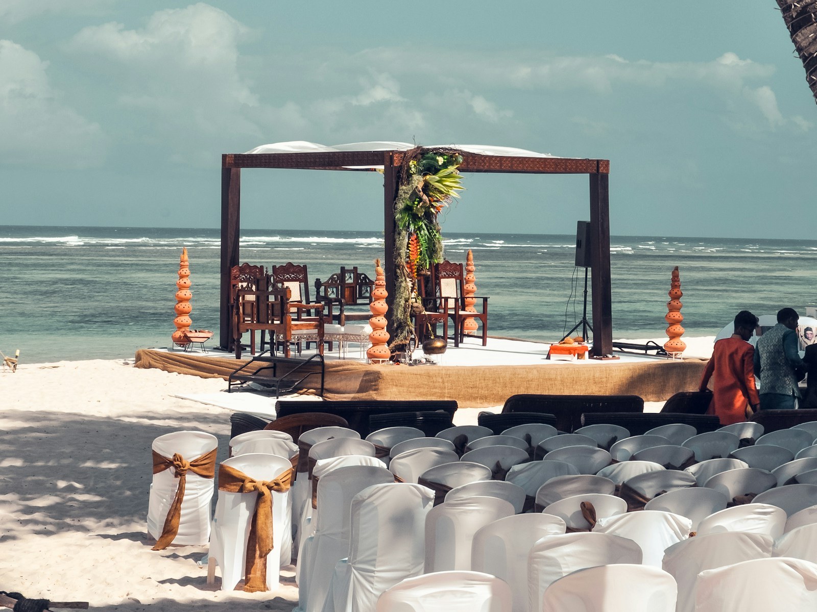 Wooden mandap set up for a destination wedding on a tropical beach, with palm trees and the ocean behind
