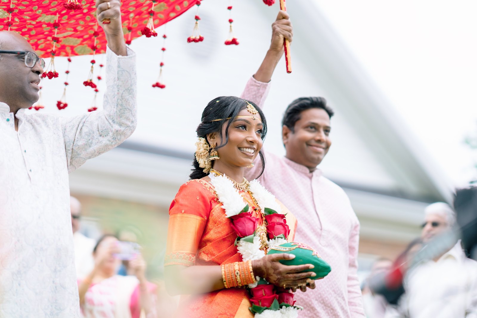 Bride smiling as she walks in beneath a red floral canopy