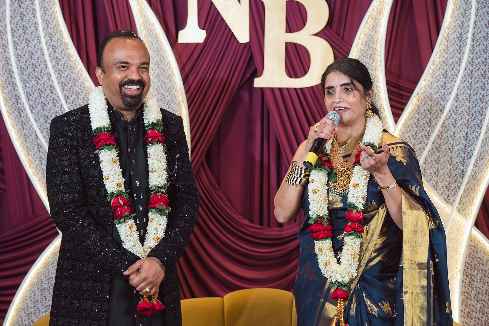 Couple wearing garlands in front of a monogram stage