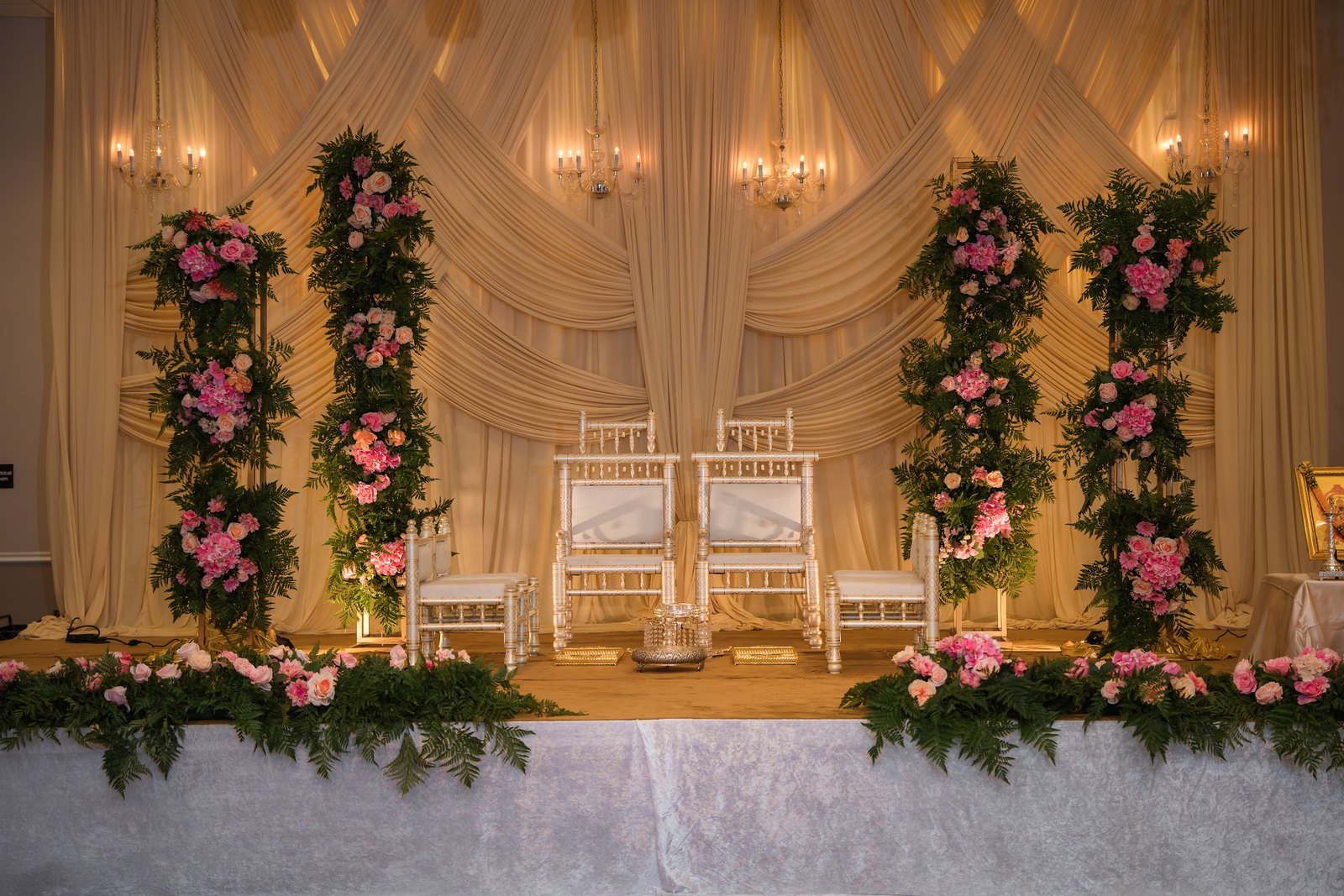 Ivory draped stage with pink floral pillars and white chairs