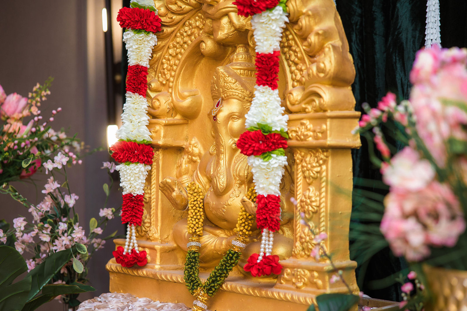 Close-up of a gold Ganesha framed by red and white flower garlands