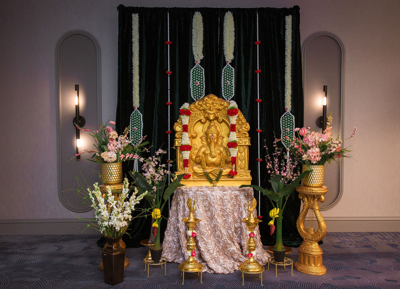 Gold Ganesha on a green velvet backdrop with jasmine garlands and pink florals