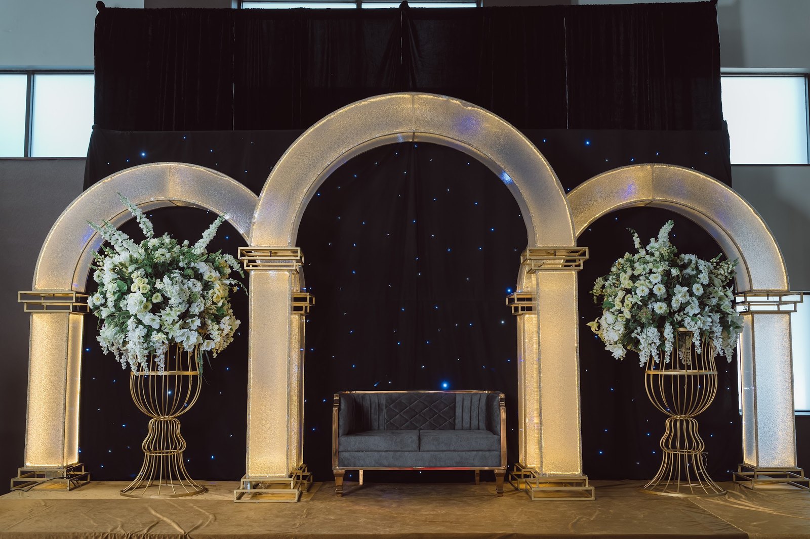 Lit gold arches with white florals on a starry black backdrop