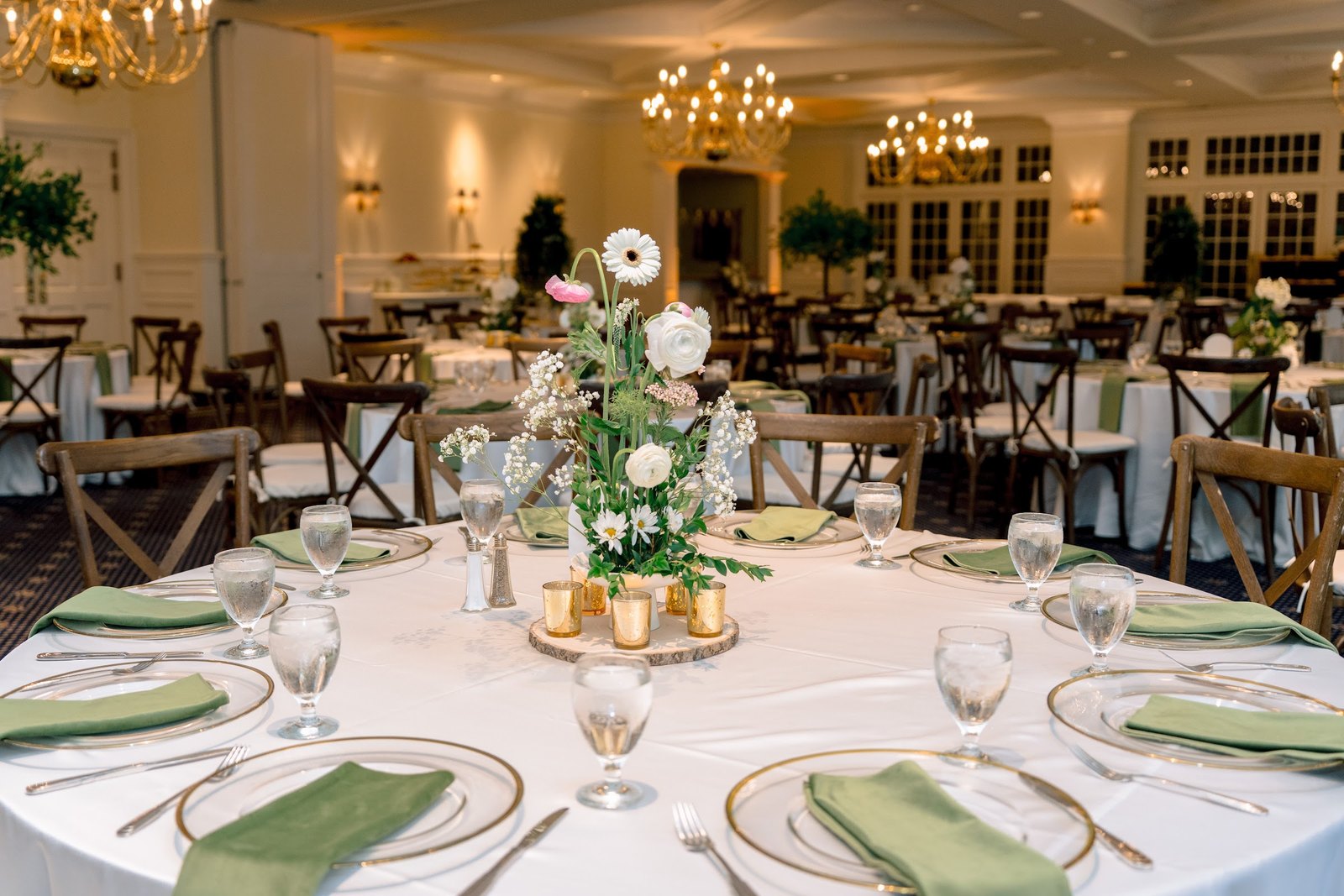 Round table with olive napkins, gold chargers and a floral centerpiece