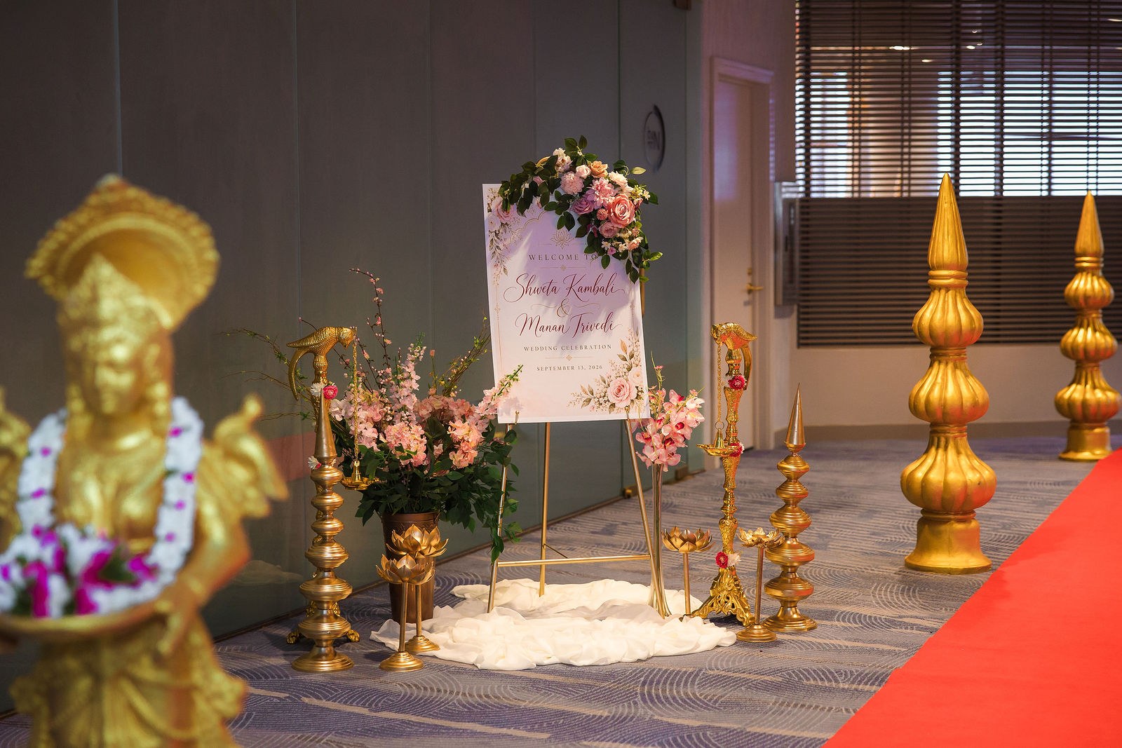 Floral wedding welcome sign with brass lamps, lotus urns and a gold statue in the foreground