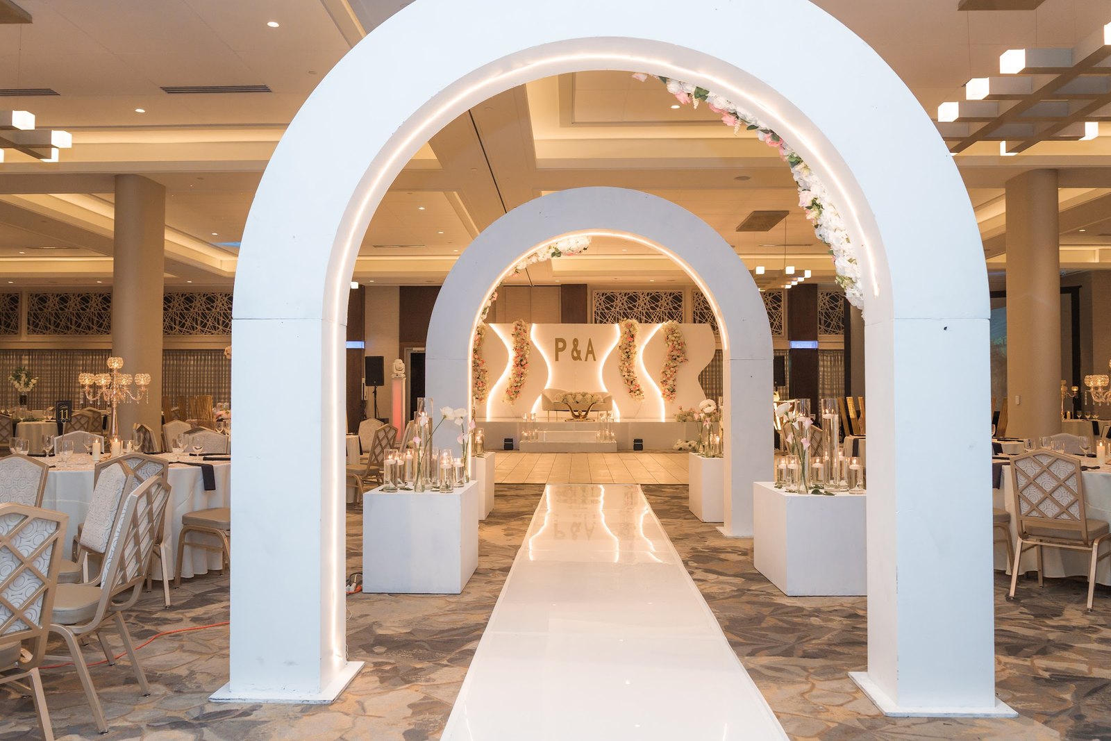 Illuminated white arches with florals leading to the reception stage
